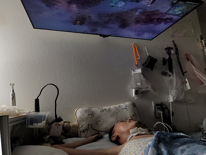 Paul lying in bed, playing Dota 2 with an overhead TV screen in front of him.